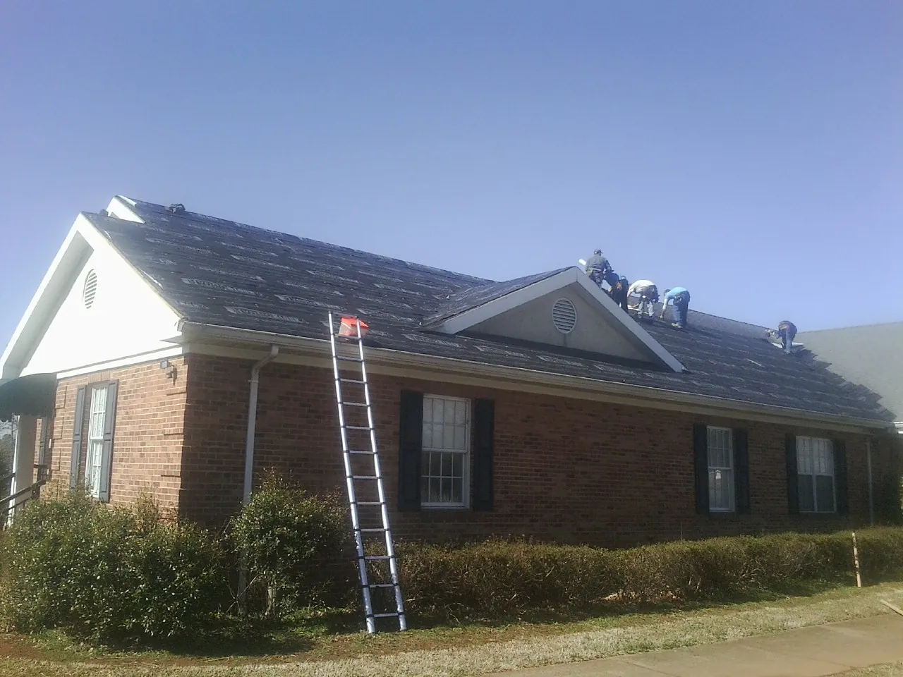 Crew tearing shingles off a brick ranch roof with a ladder set — Emergency Roof Repair work by our crew in Aldie