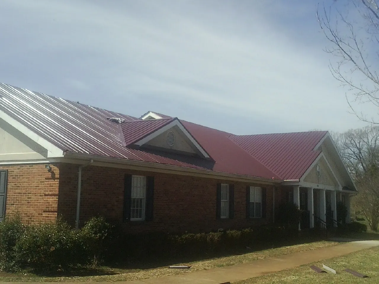 Red metal roof with gabled entries on a long brick building, from a Hail Damage Roof Repair job in Aldie
