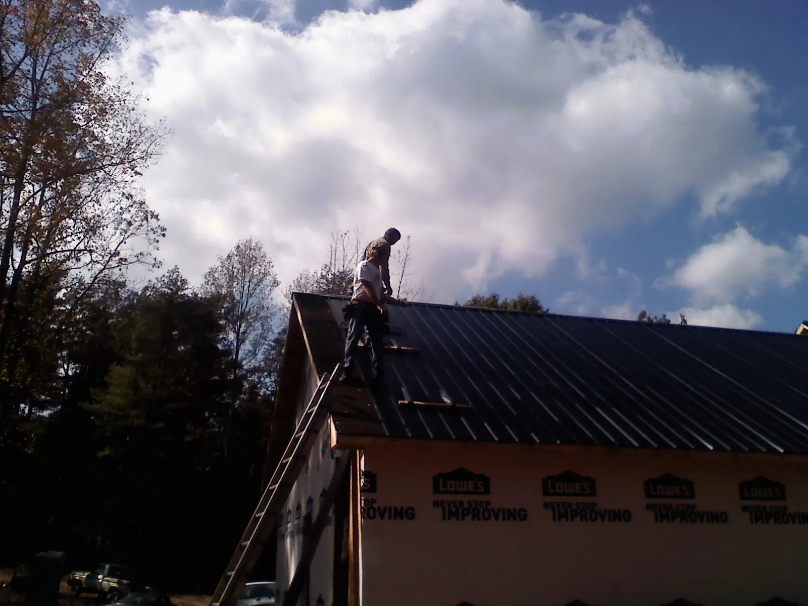 Roofer fastening dark metal panels high against a cloudy sky, from a Roof Inspection job in Aldie